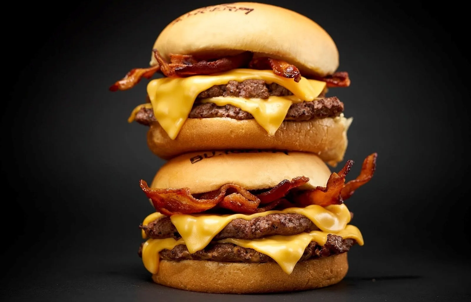 A double bacon cheeseburger with melted american cheese and crispy bacon, stacked high on a black background.